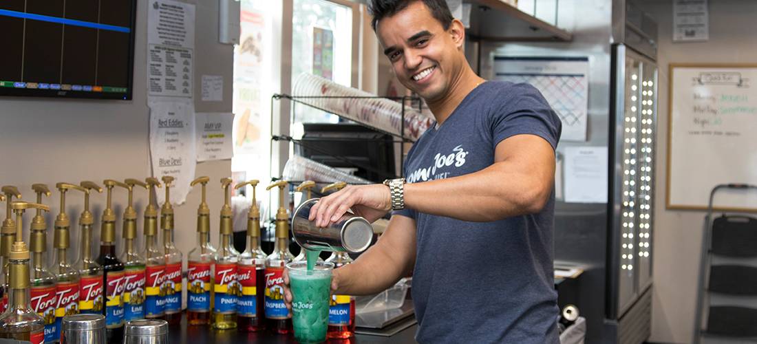 An employee at Aroma Joe’s smiling and pouring an AJ’s Energy Drink into a cup.