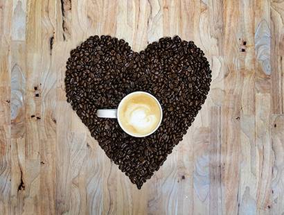 a cup of coffee in the middle of coffee beans that are in the shape of a heart