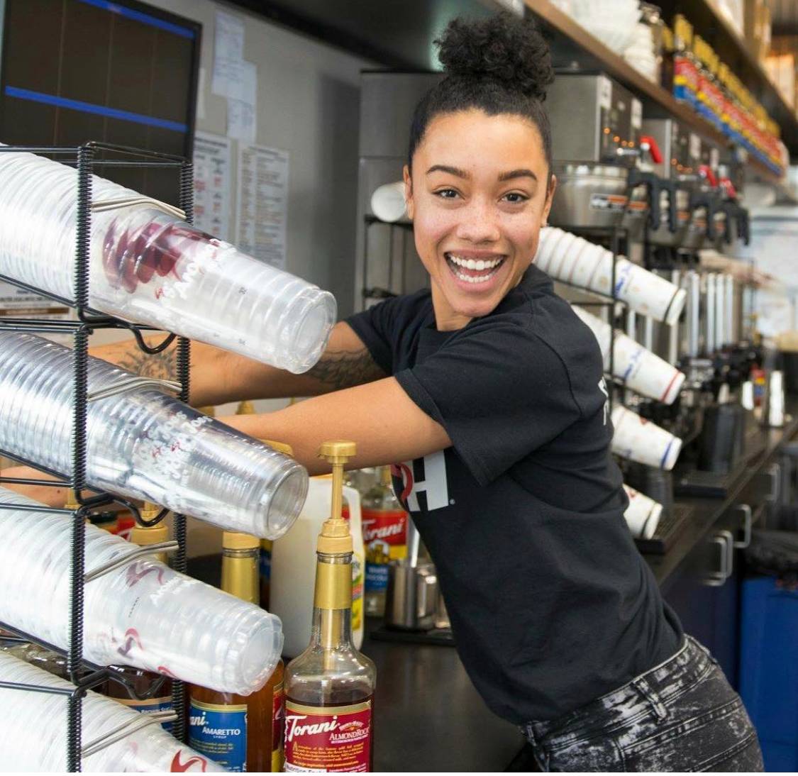 An employee of Aroma Joe’s smiling and making a cup of coffee.