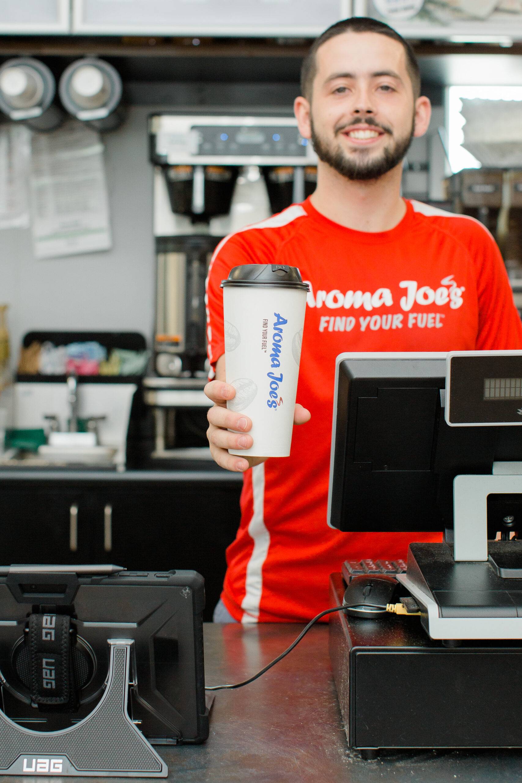 Aroma Joe’s employee behind the register handing out a coffee.