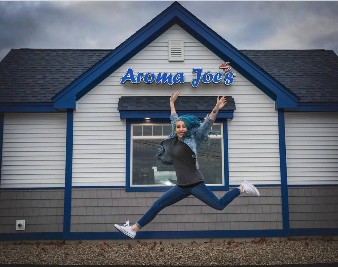 a person leaping in the air in front of an Aroma Joe’s franchise location.