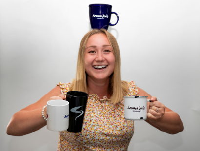 An employee of Aroma Joe’s corporate office holding three mugs and balancing another mug on her head.
